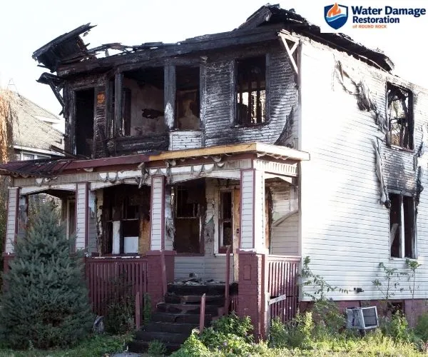 view of a two-story residential home severely charred with extensive roof collapse and burned siding from fire damage