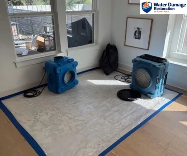 Two blue air scrubbers setup on protective floor covering in a bright room with windows.