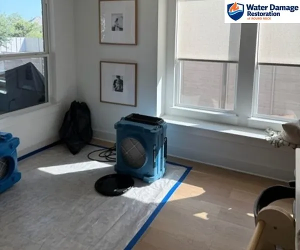 Blue air scrubber drying equipment sitting on taped floor protection next to a sunlit window.